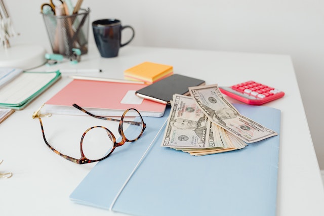 some cash, eye glasses and folders on a desk